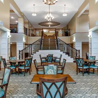 Spacious and elegant lobby area with tables, chairs, chandeliers, and a grand staircase.