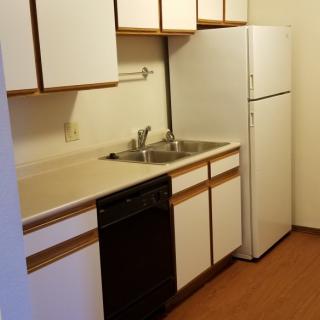 A compact apartment kitchen with white cabinets and standard appliances.