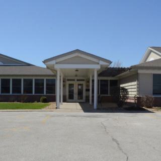 A school building with a central entrance, featuring a covered walkway and surrounding windows, captured during daytime.