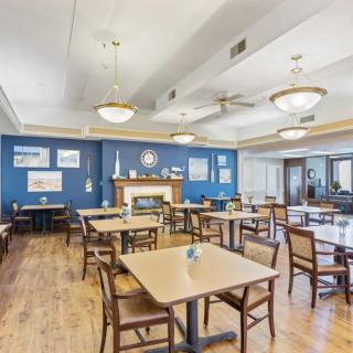 A spacious dining room with wooden floors, tables, and chairs set against a blue accent wall adorned with art.