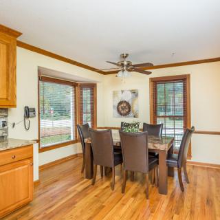 A cozy dining area with a wooden dining table and chairs, featuring hardwood flooring and ample natural light from multiple windows.
