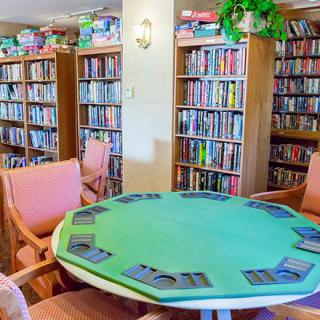 A cozy library space featuring shelves filled with books and a round table with chairs, arranged for a card game.