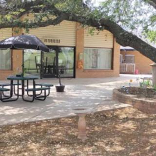An outdoor patio with a picnic table and umbrella near a building, shaded by trees.