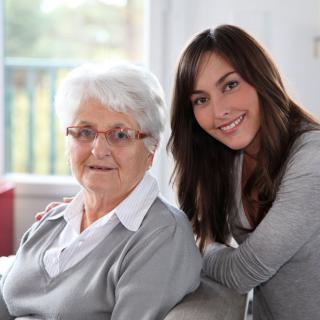 A young woman and an elderly woman smiling together indoors.