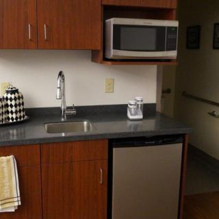 A compact kitchen area featuring a microwave, sink, small fridge, and cabinetry.