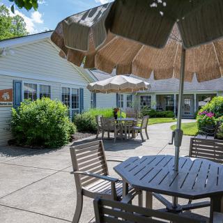 A sunny patio area with tables, chairs, and umbrellas surrounded by greenery.