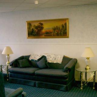 A cozy living room with a dark green sofa, two lamps on side tables, and a landscape painting on the wall.