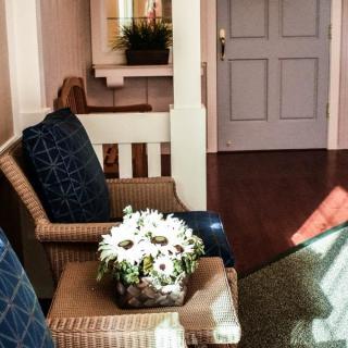 A cozy interior with wicker chairs, a table adorned with flowers, and sunlight streaming in.