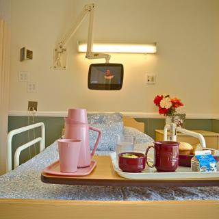 A hospital room with a bed, a meal tray with cups and flowers, and a wall-mounted television.