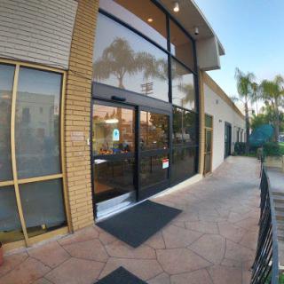 A modern storefront with large glass doors and a welcoming entrance, surrounded by palm trees.