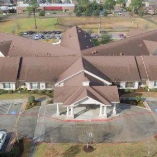 Aerial view of a large suburban building with a parking lot and surrounding greenery.