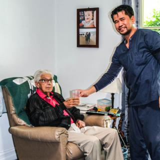 A caregiver assisting an elderly person in a living room setting.