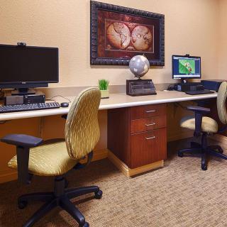 A neatly organized office space with two computers set up on a long desk, accompanied by comfortable chairs and decorated with wall art.
