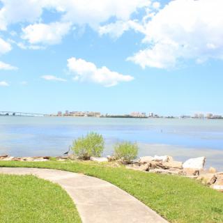 A serene view of a lakeside pathway under a bright, cloudy sky.