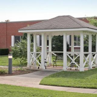 A white gazebo situated in a landscaped garden area with a paved pathway and surrounding greenery.