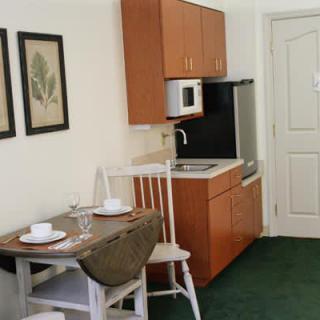 A compact kitchen and dining area featuring a small table with chairs, cabinetry, sink, microwave, and framed artwork on the wall.