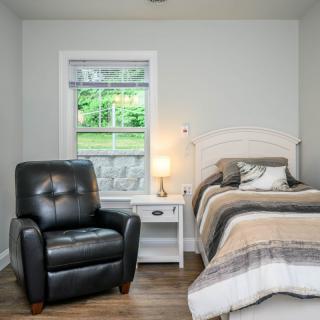 Cozy bedroom with a recliner, bed, and nightstand under a window.