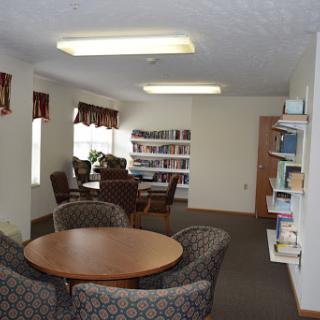 A cozy reading area featuring plush chairs, a circular table, and shelves filled with books.