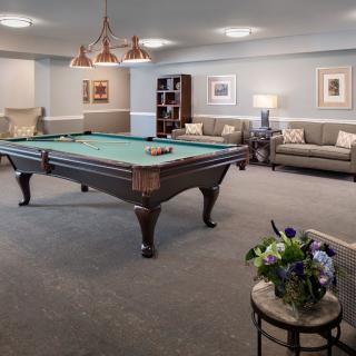 A cozy billiard room featuring a central pool table, comfortable sofas, elegant lighting, and tasteful decor.