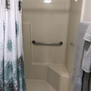 A bathroom with a shower equipped with a grab bar and patterned shower curtain.