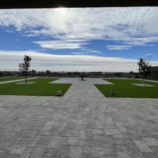 A serene outdoor landscape featuring a stone pathway bordered by lush greenery and trees under a partly cloudy sky.