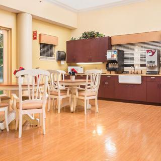 A cozy dining area with several tables and chairs, featuring a wooden floor and a counter with a coffee machine.
