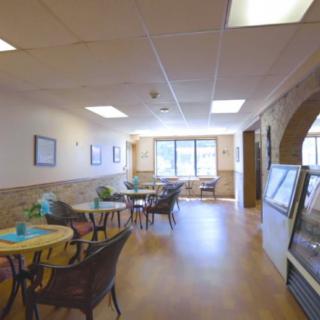 A cozy cafe with tables and chairs arranged near large windows, allowing natural light to brighten the space.