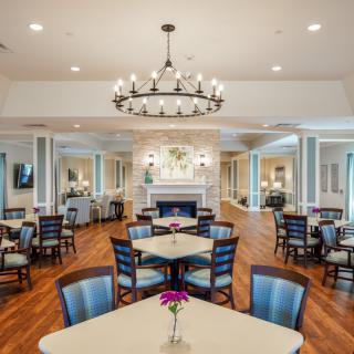 An elegantly designed dining room featuring a large chandelier, a central fireplace, and neatly arranged tables and chairs.