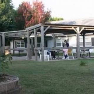 A backyard scene featuring a pergola with chairs and people enjoying the outdoor area.