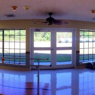 A sunlit interior room with large windows and glass doors, featuring a ceiling fan.