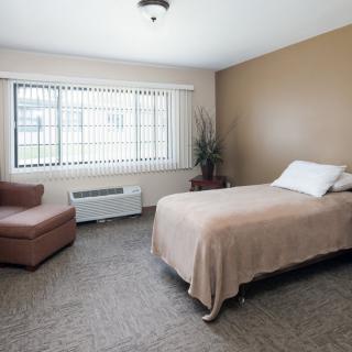 A minimalist bedroom with a single bed, beige decor, and large windows.