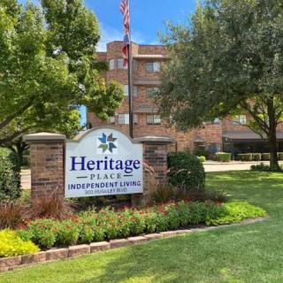 A sign for Heritage Place Independent Living in front of a building surrounded by trees and a well-maintained lawn.