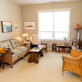 A cozy living room with a sofa, armchair, and coffee table, decorated with artwork and a lamp.