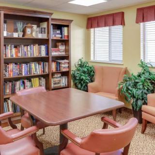 A cozy library room with a wooden table, chairs, bookshelves, and indoor plants.