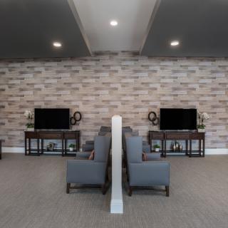 A modern living room featuring a symmetrical arrangement with TVs and armchairs against a stylish brick wall.