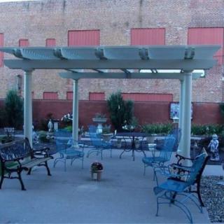 A cozy outdoor patio with a pergola, surrounded by chairs and benches, set against a brick wall.