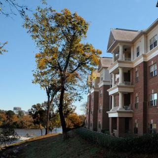A view of an apartment building with balconies overlooking a river, surrounded by trees with autumn foliage.