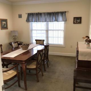 A cozy dining room with a wooden table and chairs, featuring a large window with blue curtains.