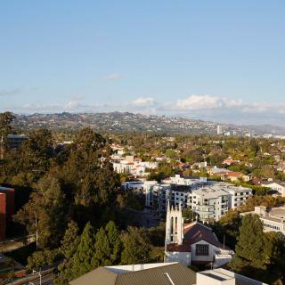 A scenic view of an urban landscape with distant mountains, featuring buildings and lush greenery under a clear blue sky.