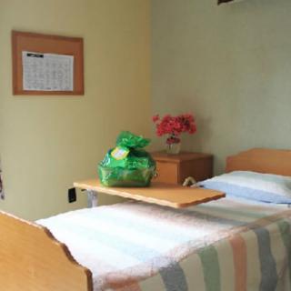 A hospital room with a bed, flowers, and a gift on the tray table.