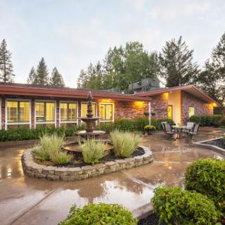 A tranquil outdoor setting featuring a charming building, a fountain, and beautifully landscaped gardens.
