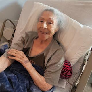 An elderly woman smiling while resting in bed.