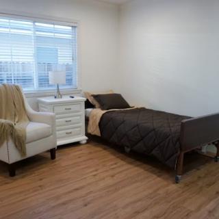A minimalist bedroom with a single bed, armchair, and nightstand by the window.