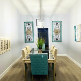 A stylish dining room with modern decor featuring turquoise chairs and a glass table, complemented by contemporary wall art and indoor plants.