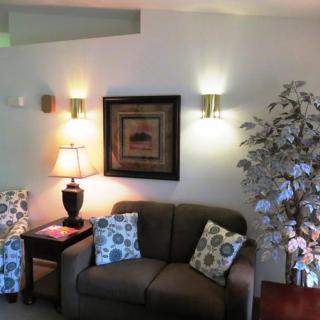 A cozy living room with a sofa, decorative cushions, a floor lamp, wall art, and an indoor plant.