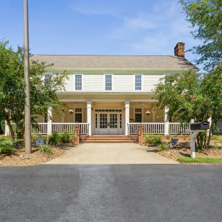 A charming two-story house with a front porch and surrounding greenery.