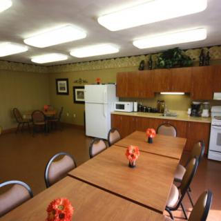 A communal kitchen and dining area with tables, chairs, a refrigerator, microwave, and decorative flowers.