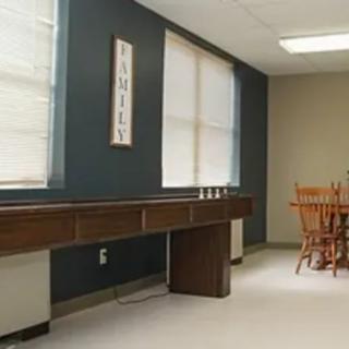 A simple room interior featuring a long wooden shelf and a dining table with chairs.