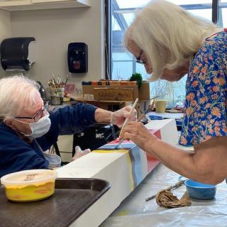 Two seniors engaged in a collaborative painting project during an art workshop.