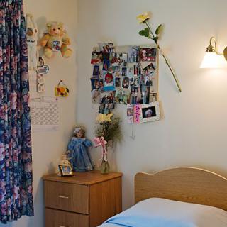 A cozy bedroom with a single bed, nightstand, and personal photos on the wall.